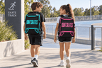 Two young skaters wearing blue-trim and pink-trim Bont backpacks at an outdoor skate track.