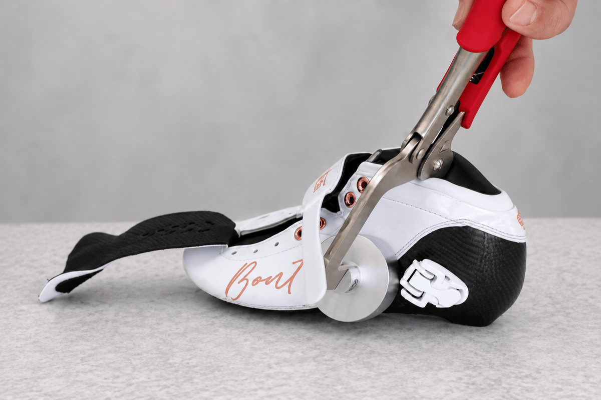 Red-grip Rip Jaws tool positioned around the heel of a white and black carbon skate boot.